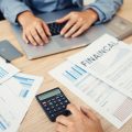 Persoană analizând documente financiare la birou.